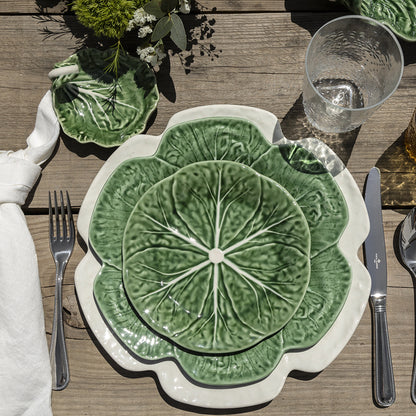 Green ceramic plate with leaf design on a wooden table setting.