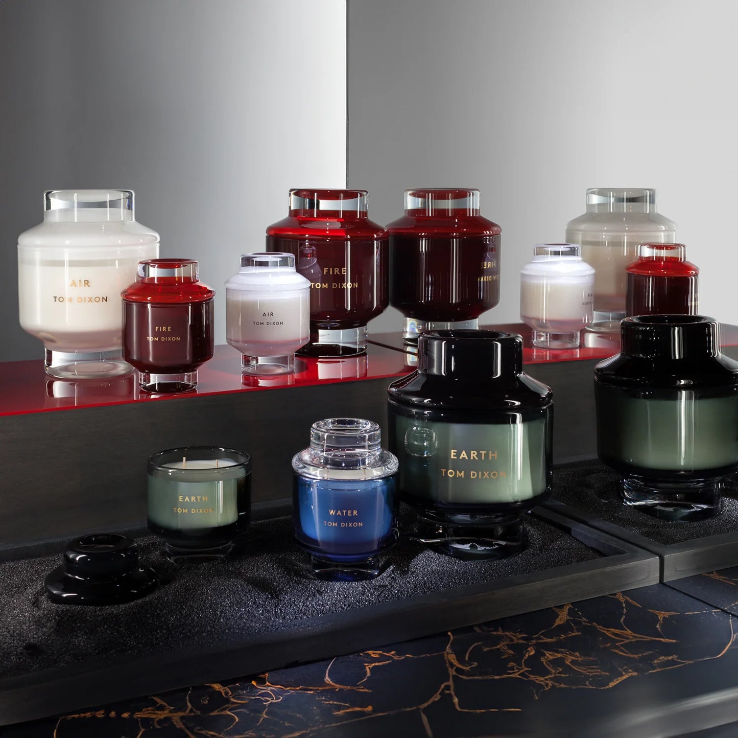 candle-Collection of candles and bottles with visible branding on a reflective surface.