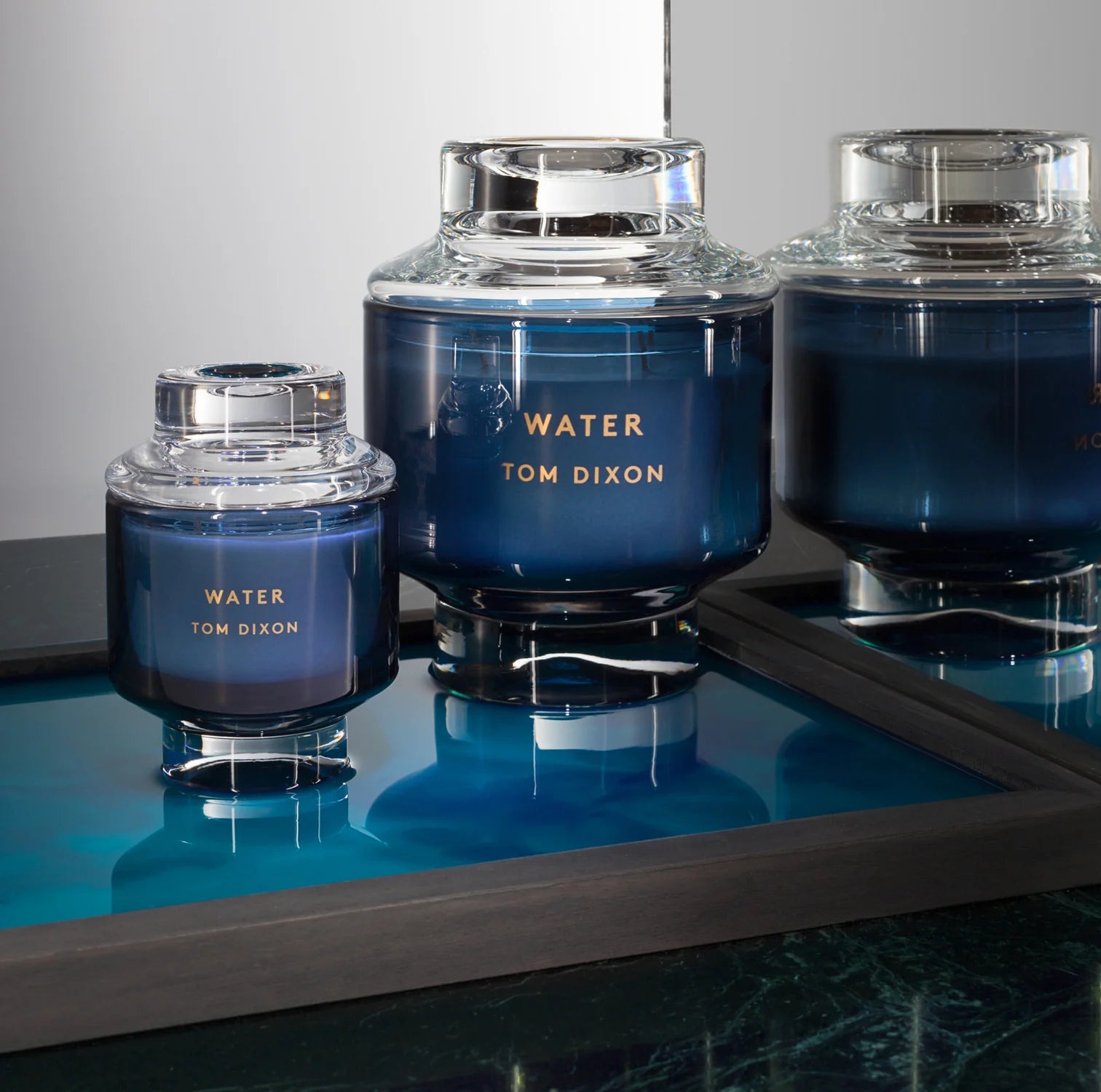 candle-Three blue glass containers with 'Tom Dixon' branding on a reflective surface.