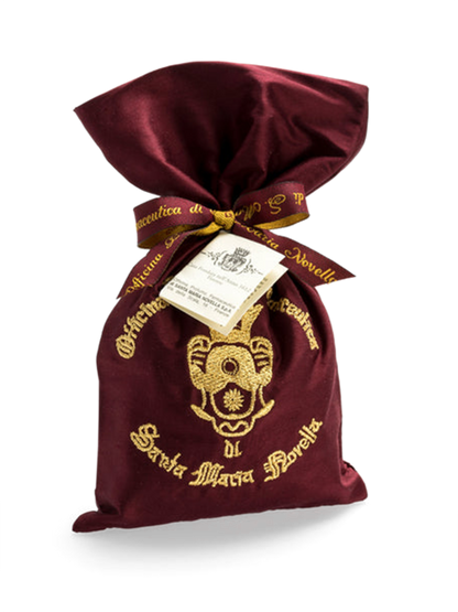 A red embroidered silk bag with gold brand embroidery and a pot pourri inside, tied with a ribbon.
