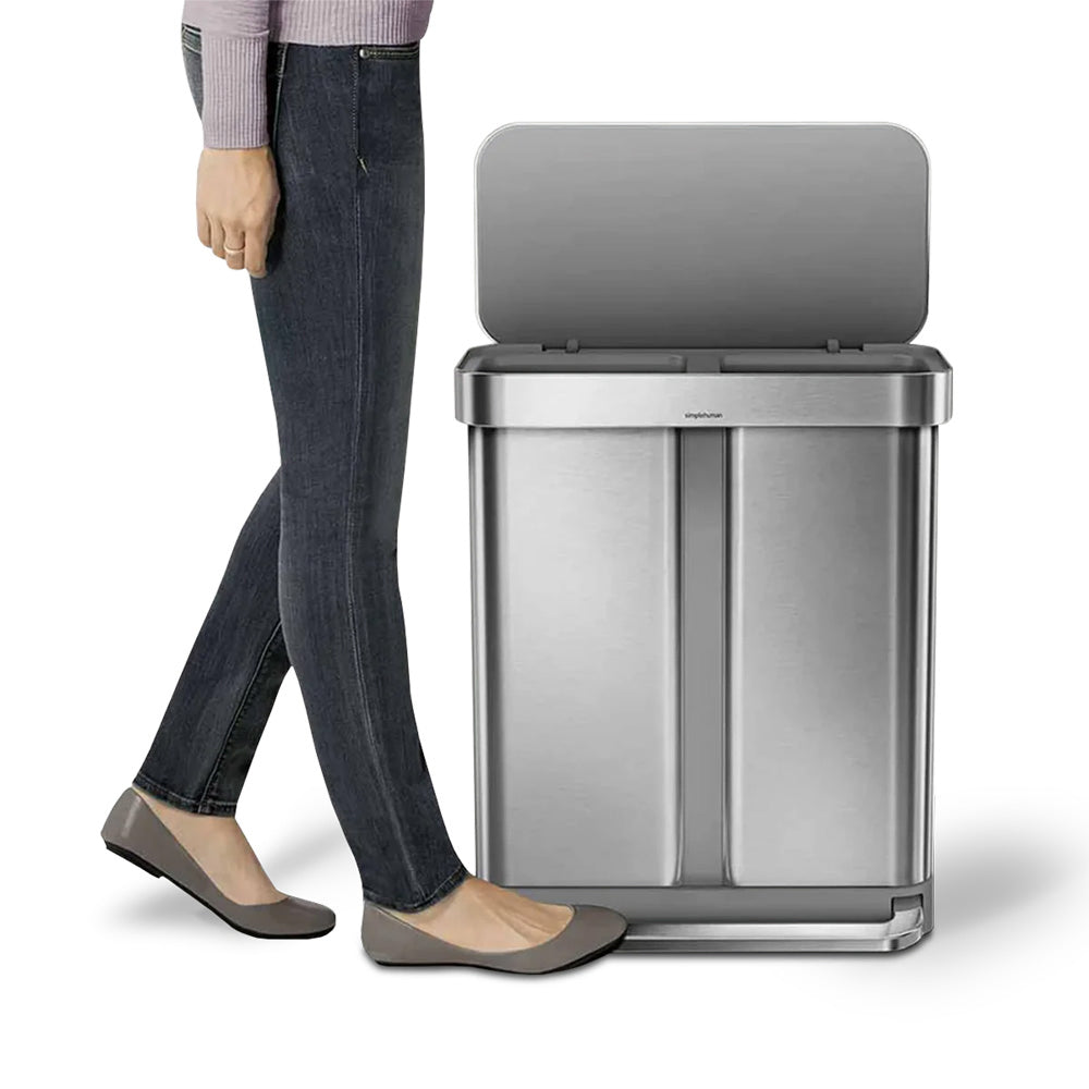 Person standing next to a large stainless steel trash can on a white background