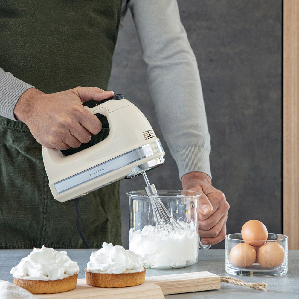 Person using a hand mixer to whip cream with eggs on the side