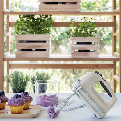 Hand mixer on a table with cupcakes and a blurred outdoor background