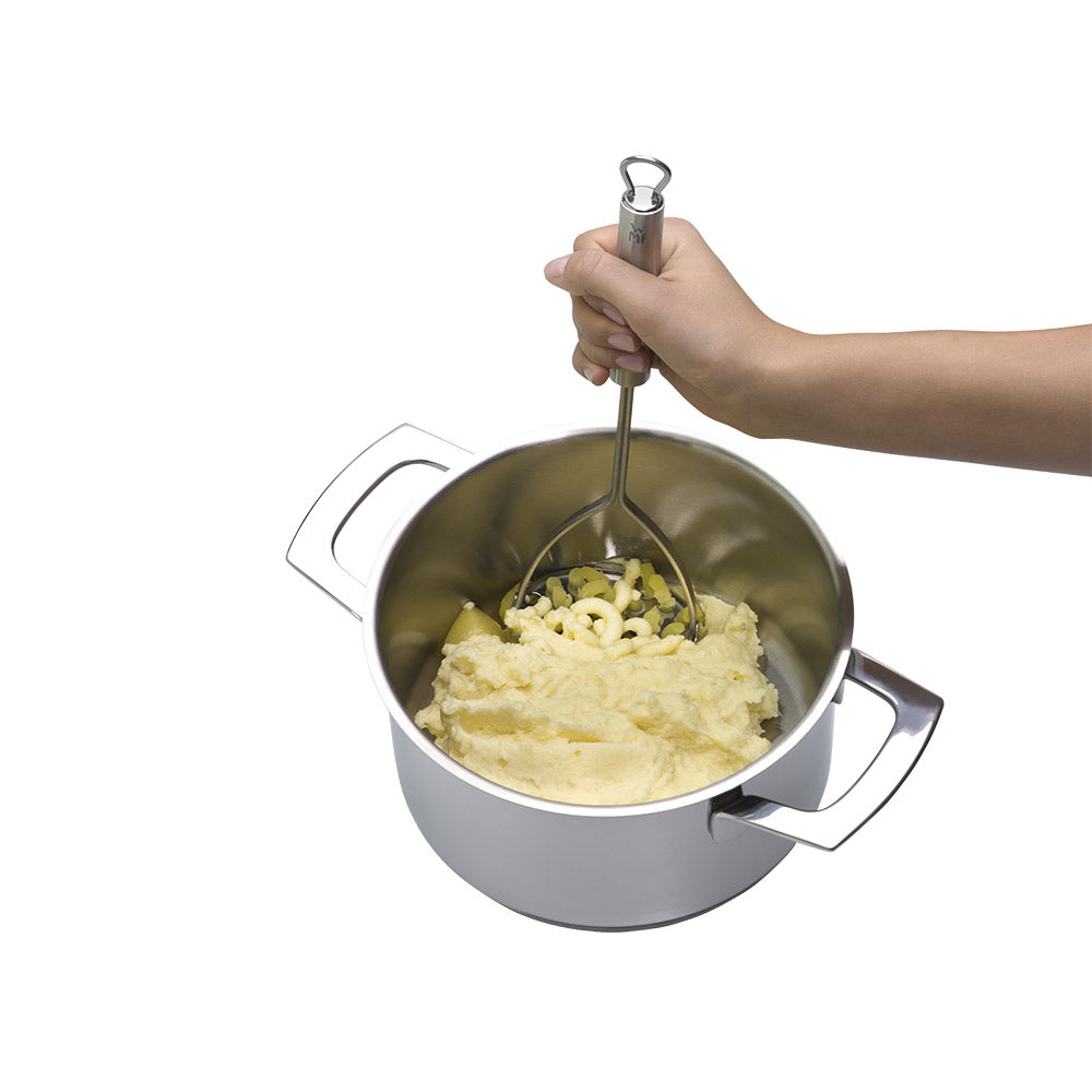 Hand using a potato masher in a pot of mashed potatoes on a kitchen utensil-