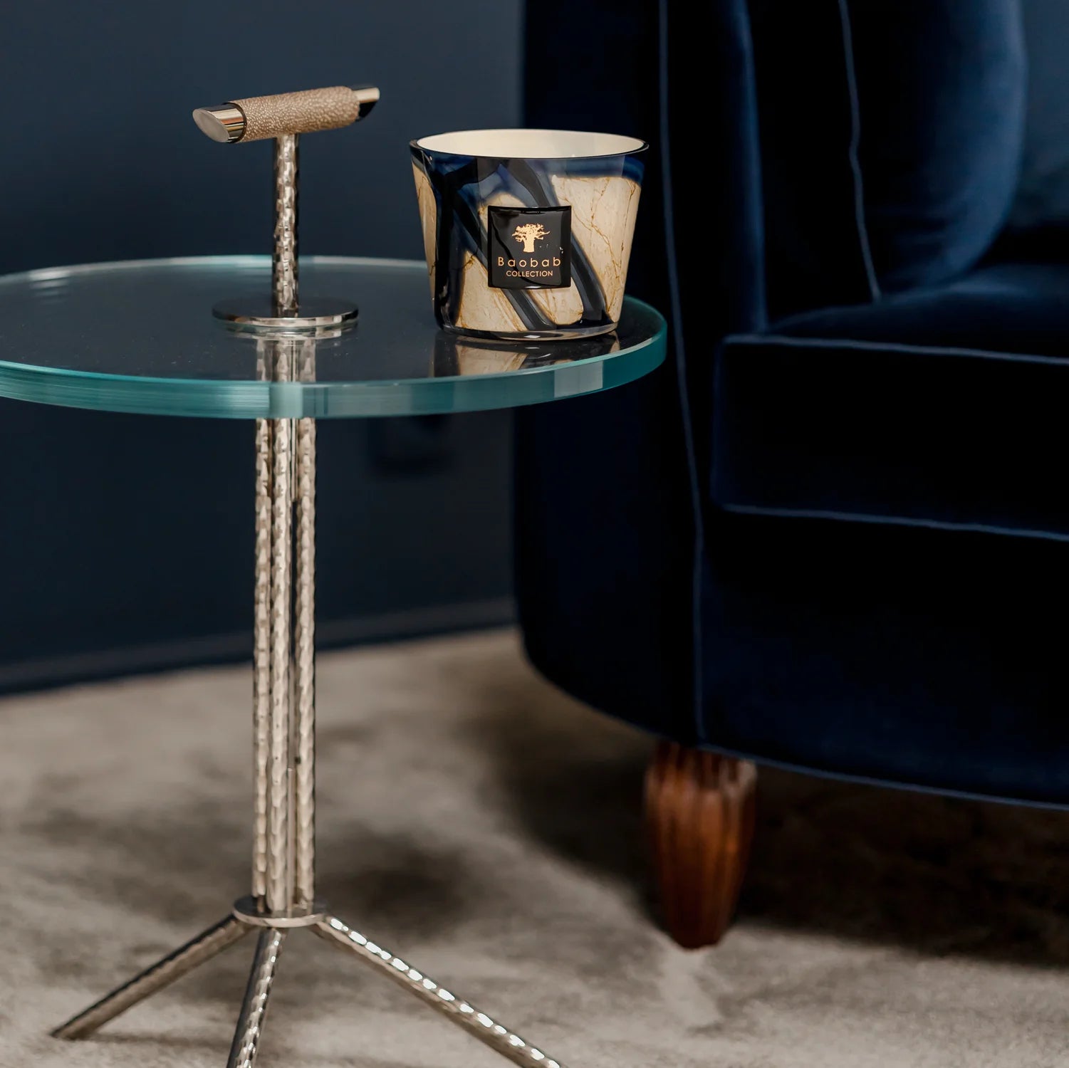 scented candles-Glass side table with decorative item next to a blue velvet chair