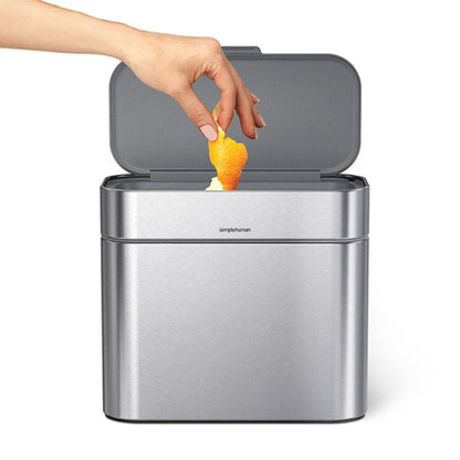 simplehuman Compost Caddy Hand disposing of an orange peel into a silver trash can with 'simplehuman' branding.