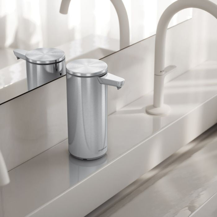 simplehuman Rechargeable Sensor Soap Pump-Silver soap dispenser on a bathroom counter with a mirror and faucet in the background