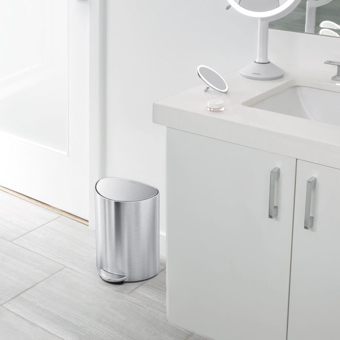 Silver trash can in a bathroom setting with a vanity and mirror.