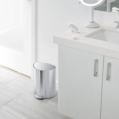 Silver trash can in a bathroom setting with a vanity and mirror.